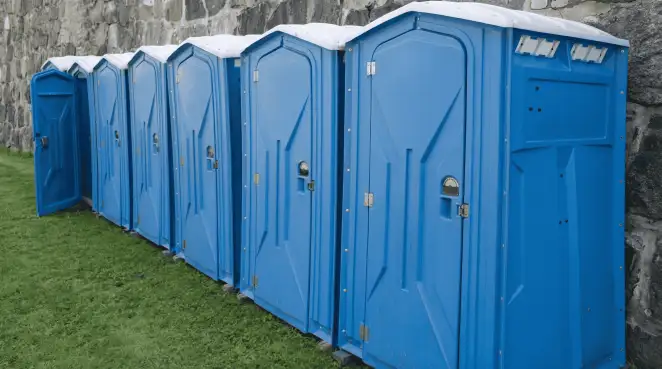 Row of blue portable toilets lined up on grass against a stone wall for event sanitation in Tampa, FL